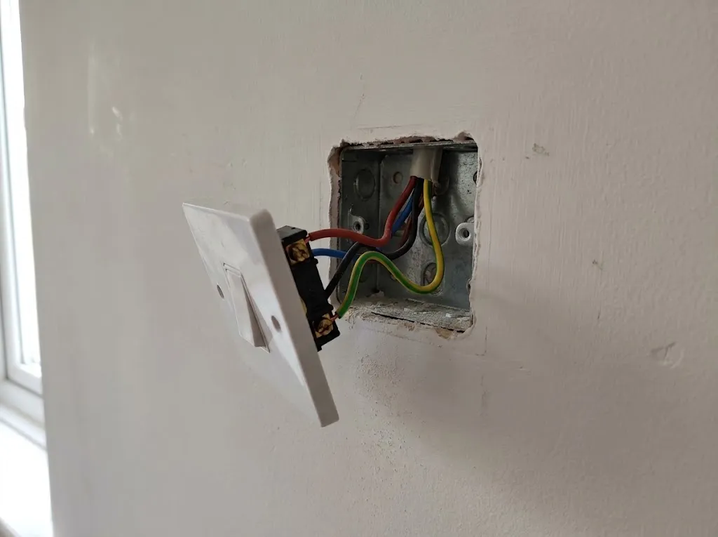 Light switch plate removed from the wall during a survey, showing the existing wiring at the back box