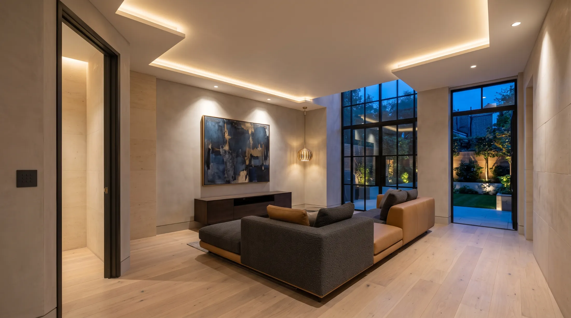Open-plan reception room at dusk with layered lighting, garden glazing and a wall keypad